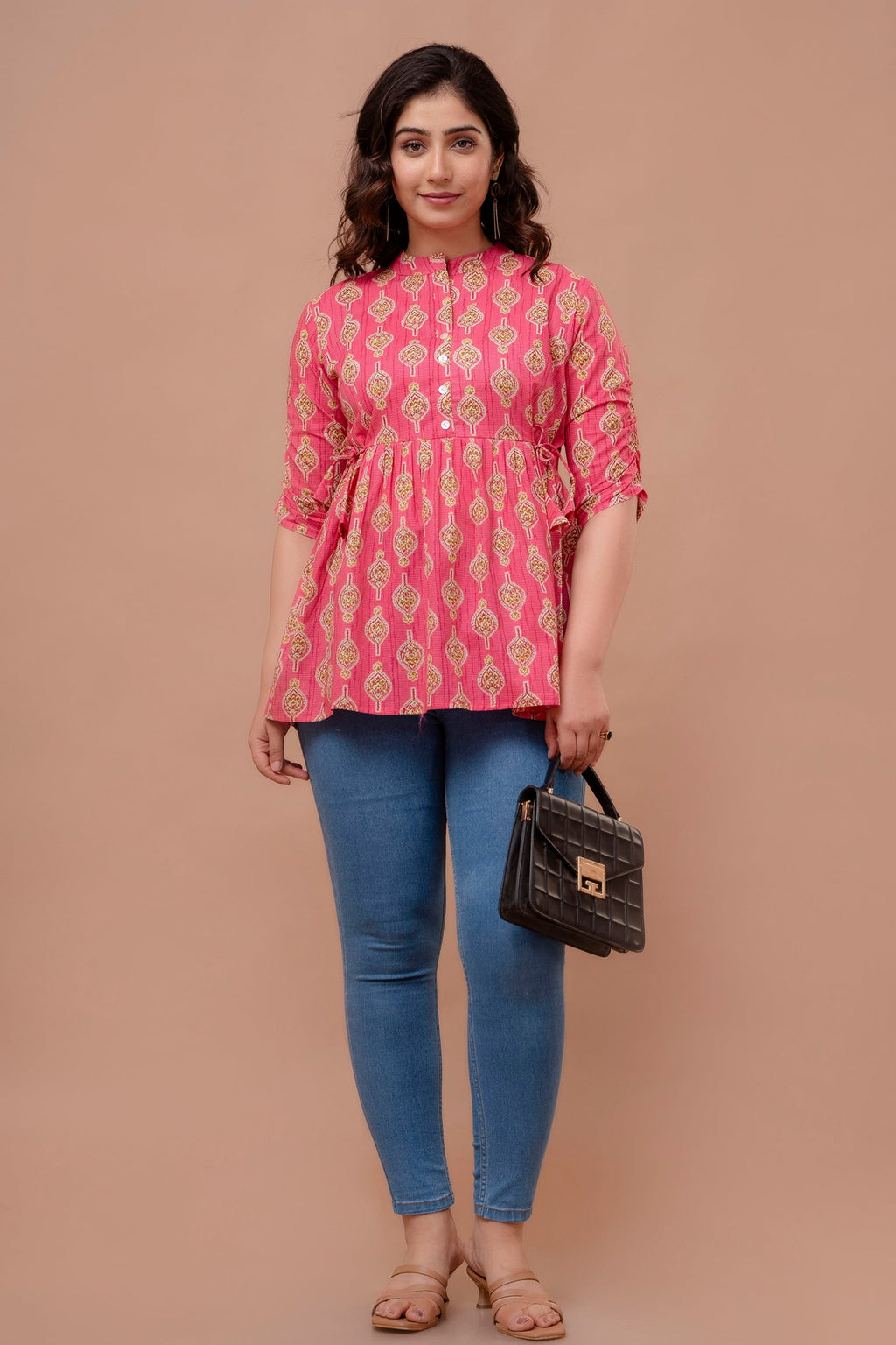 Woman wearing a pink patterned top and blue jeans, holding a black handbag on a beige background