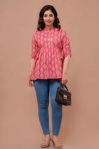 Woman wearing a pink patterned top and blue jeans, holding a black handbag on a beige background